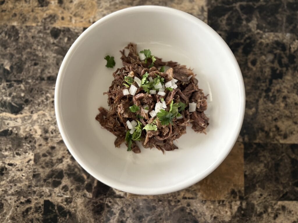 Top view of beef barbacoa garnished with cilantro and onion in a bowl.