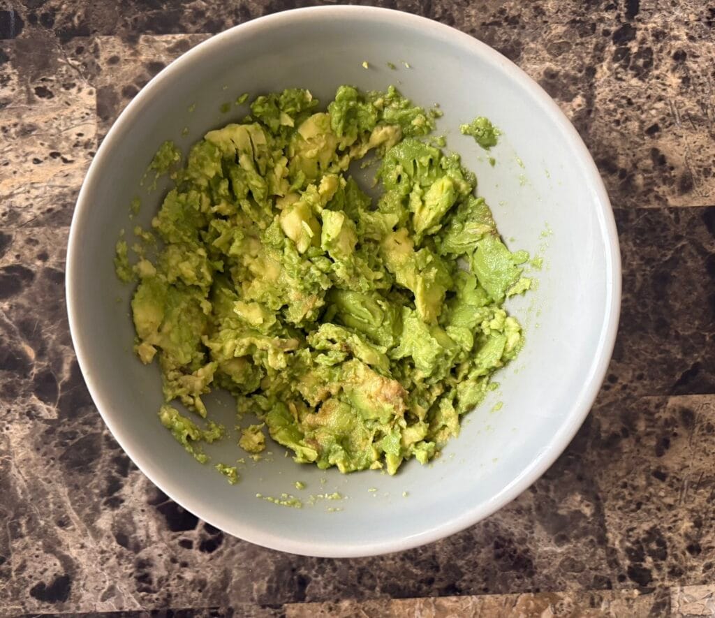 Top view of mashed avocado in bowl.
