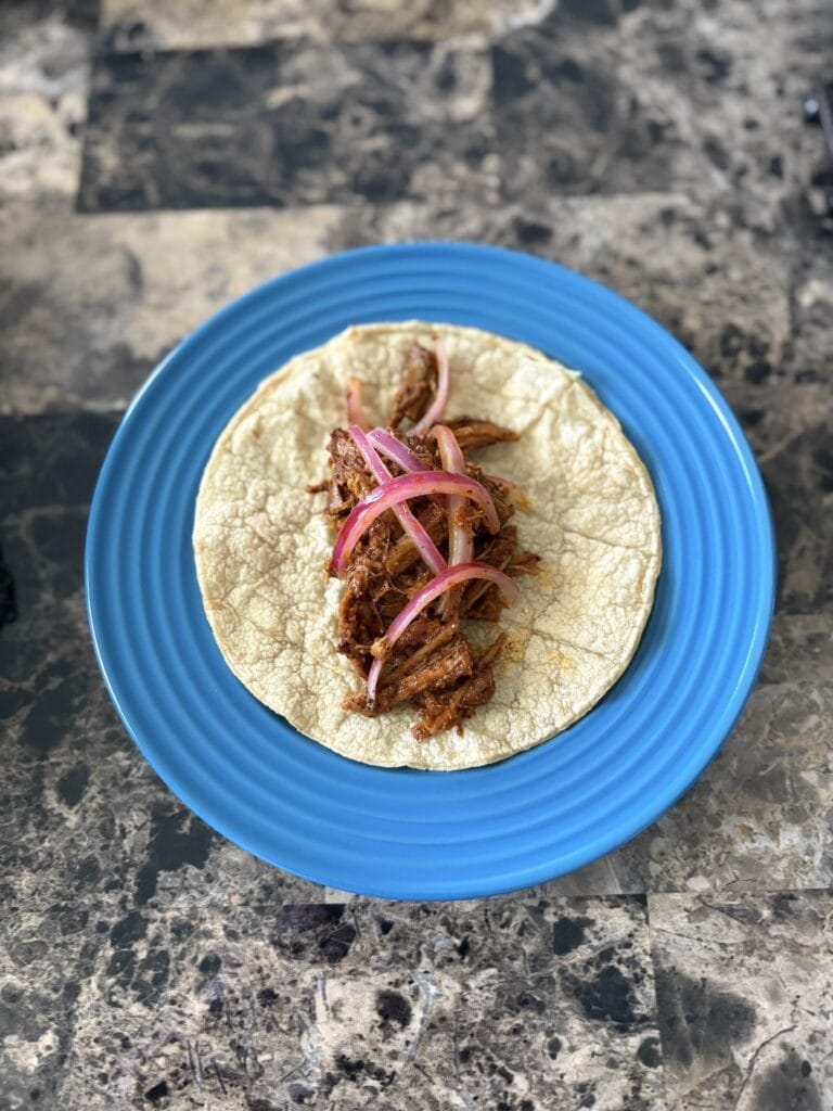 Top view of cochinita pibil taco garnished with pickled red onions on a plate.