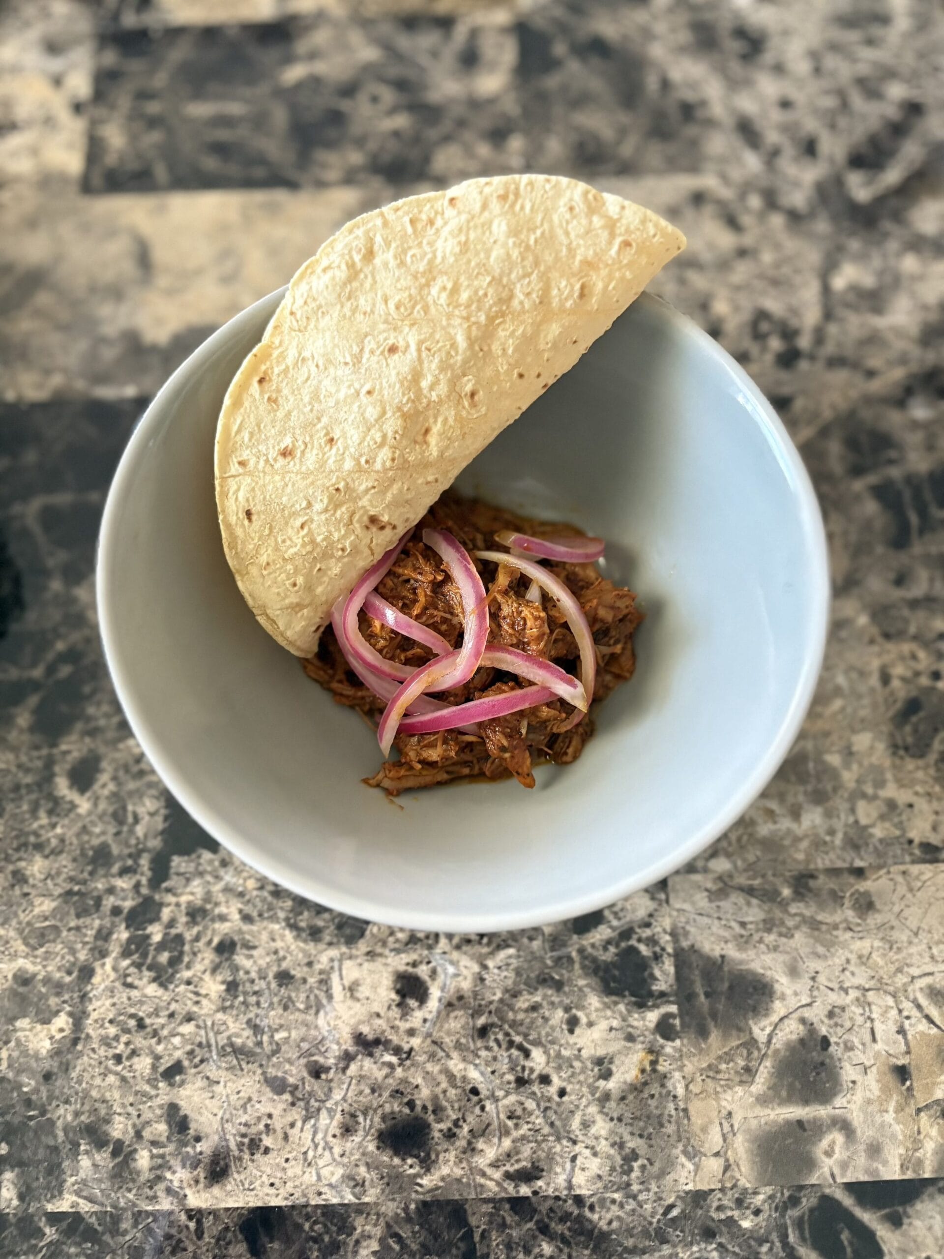 Top view of cochinita pibil garnished with pickled red onions and with a folded tortilla in a bowl.