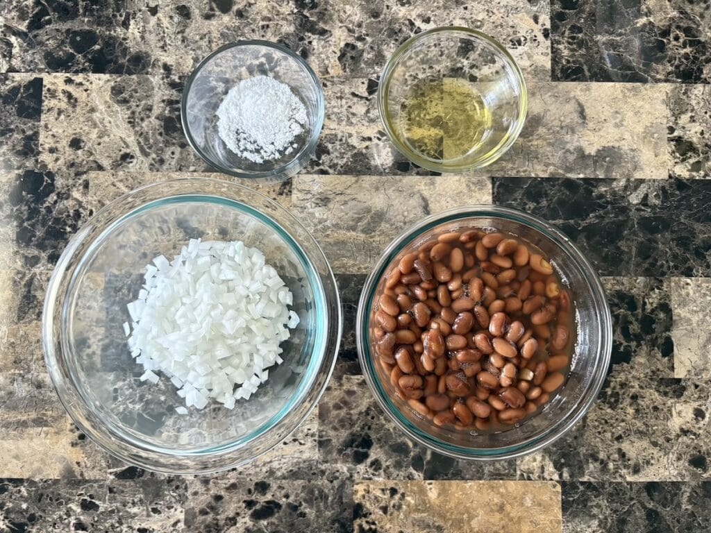 Top view of refried beans ingredients which include chopped white onion, cooked beans, salt, and cooking oil.