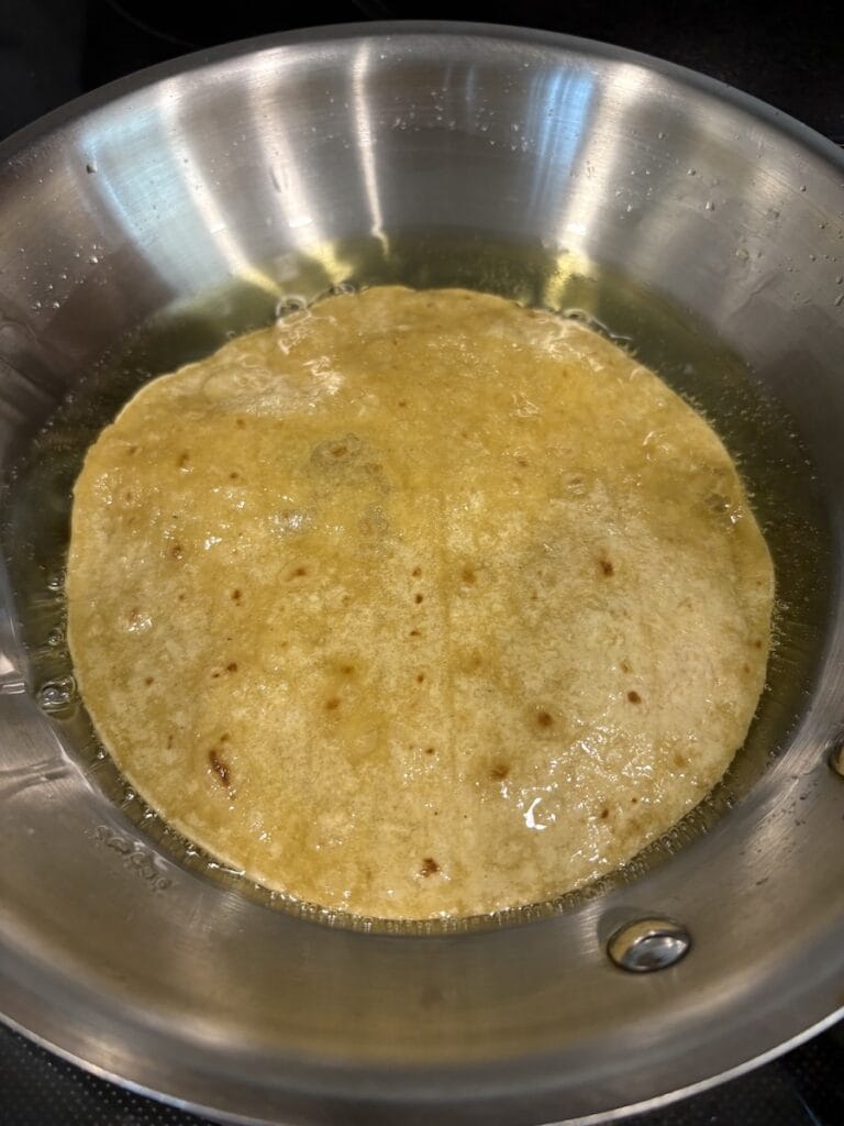 Top view of second side of tortilla fried in oil in a skillet.