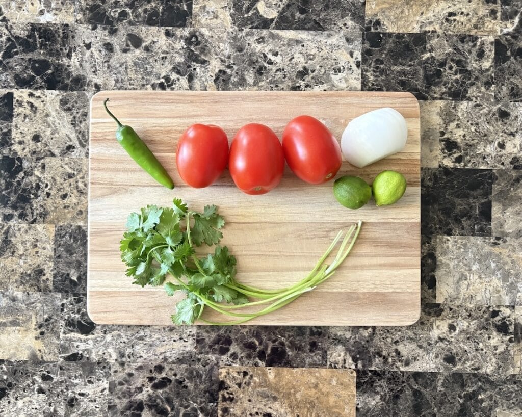 Top view of pico de gallo ingredients which consists of tomatoes, serrano chile, white onion, cilantro, and juice of limes.
