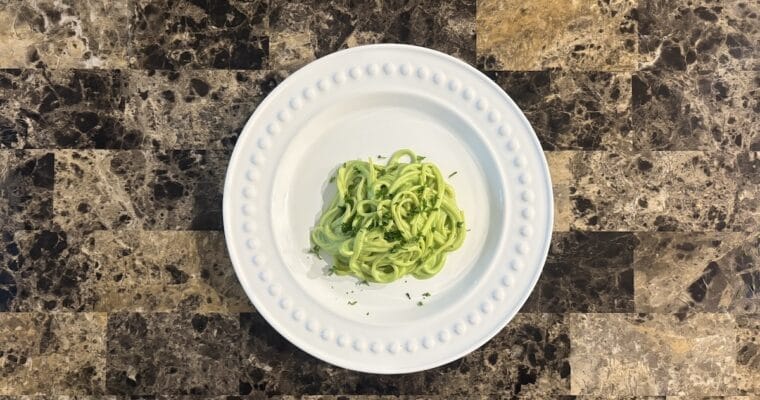 Top view of espagueti verde on a white plate garnished with chopped parsley leaves.