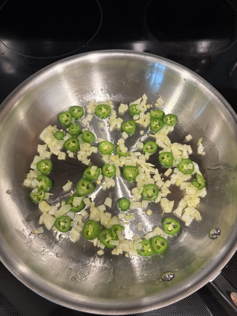 Top view of sautéed chopped white onion and sliced serrano chiles in a skillet.