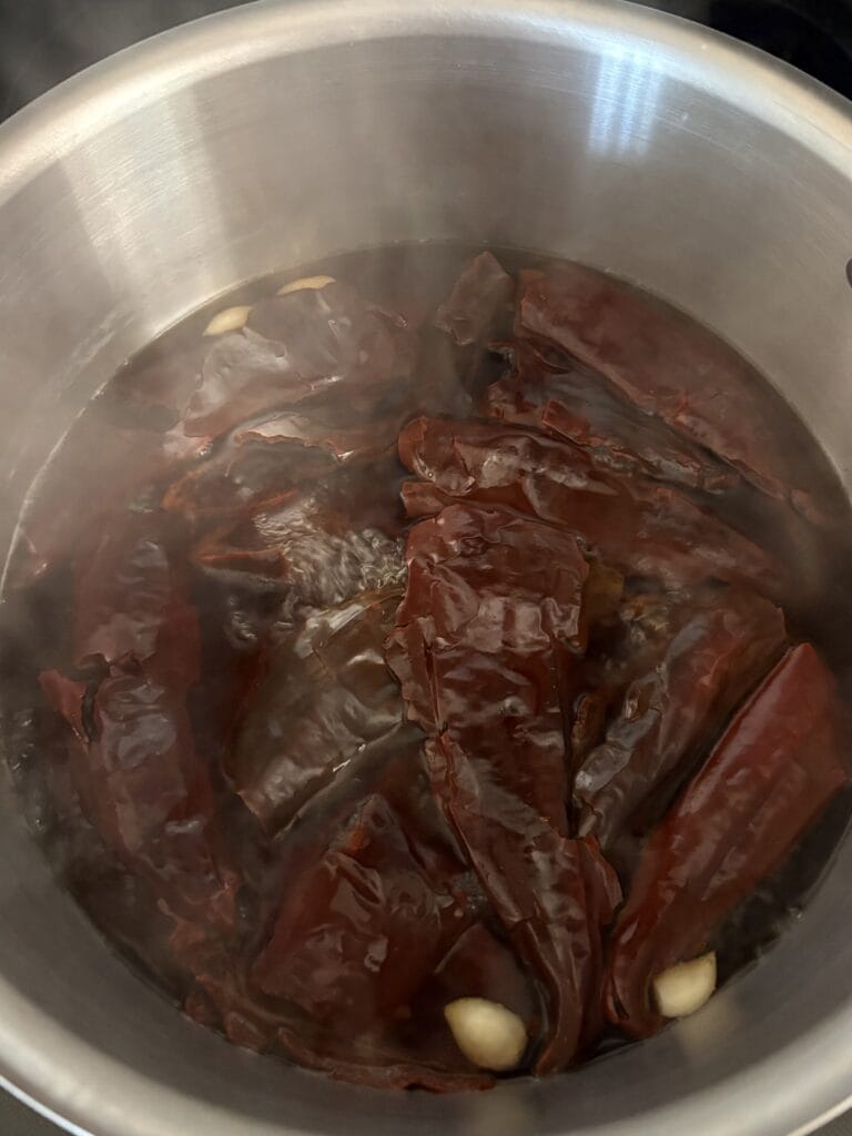 Top view of guajillo chiles and garlic simmering in a pot.
