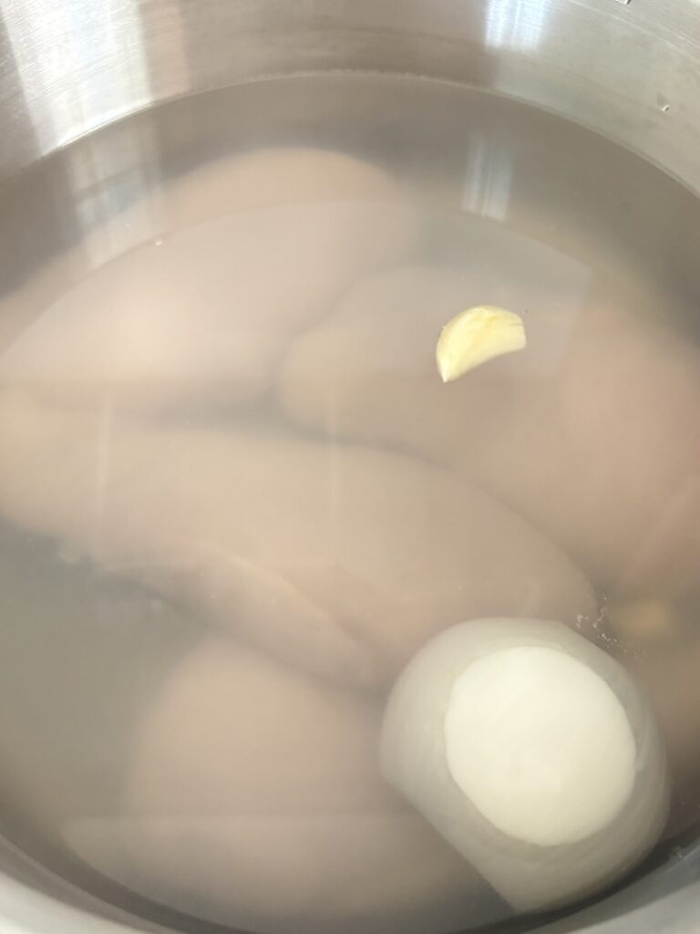 Top view of chicken breast, garlic, and onion in pot filled with water.