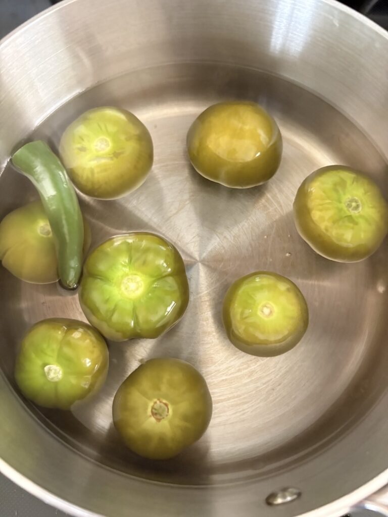 Top view of tomatillos and serrano chile simmering in a pot.